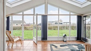 A conservatory with large glass doors, a wooden chair, and a rug. - Cozy home in Sjølund with sauna (Sjølund)