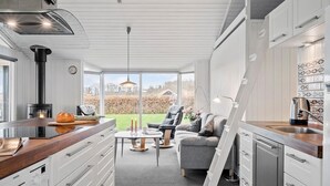 A modern kitchen with a built-in wood stove, a dining area with a table and chairs, and a view of a garden. - Cozy home in Sjølund with sauna (Sjølund)