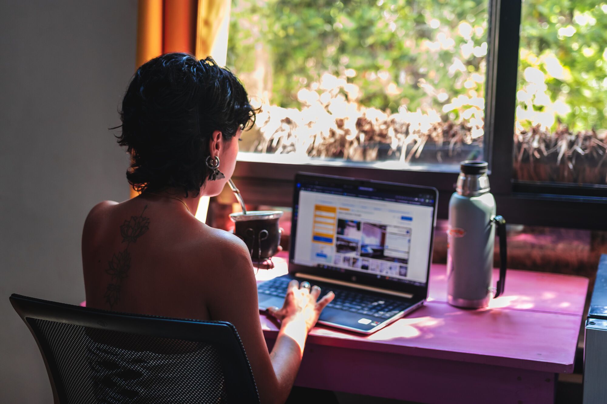 Eine Person sitzt an einem Schreibtisch mit einem Laptop, einer Tasse und einer Wasserflasche.
