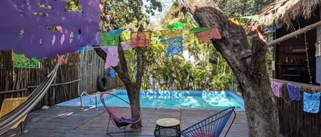 A wooden deck with two chairs, a small round table, and a pool in the background.