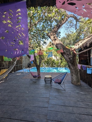 A wooden deck with two chairs, a small round table, and a pool in the background.