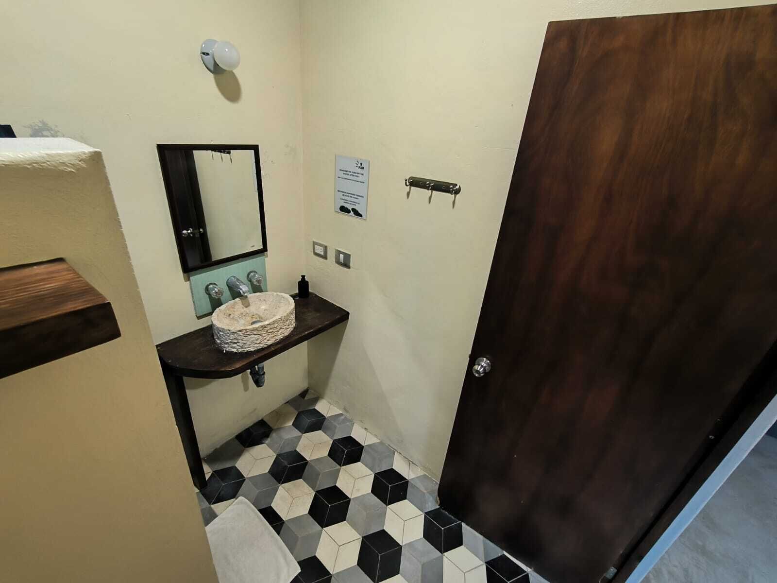 A bathroom with a hexagonal tile floor, a wooden door, a sink with a stone basin, a mirror, and a towel rack.