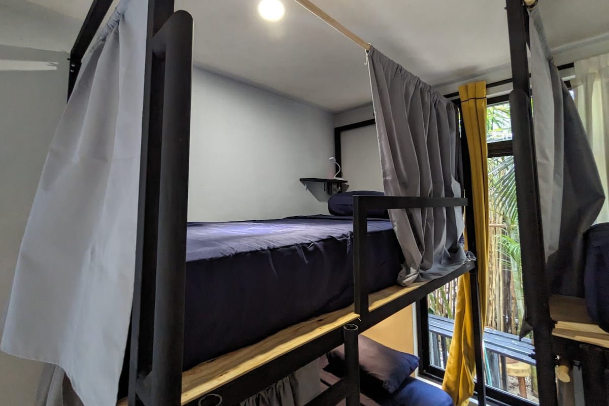 A bunk bed room with a window, curtains, and a small shelf.