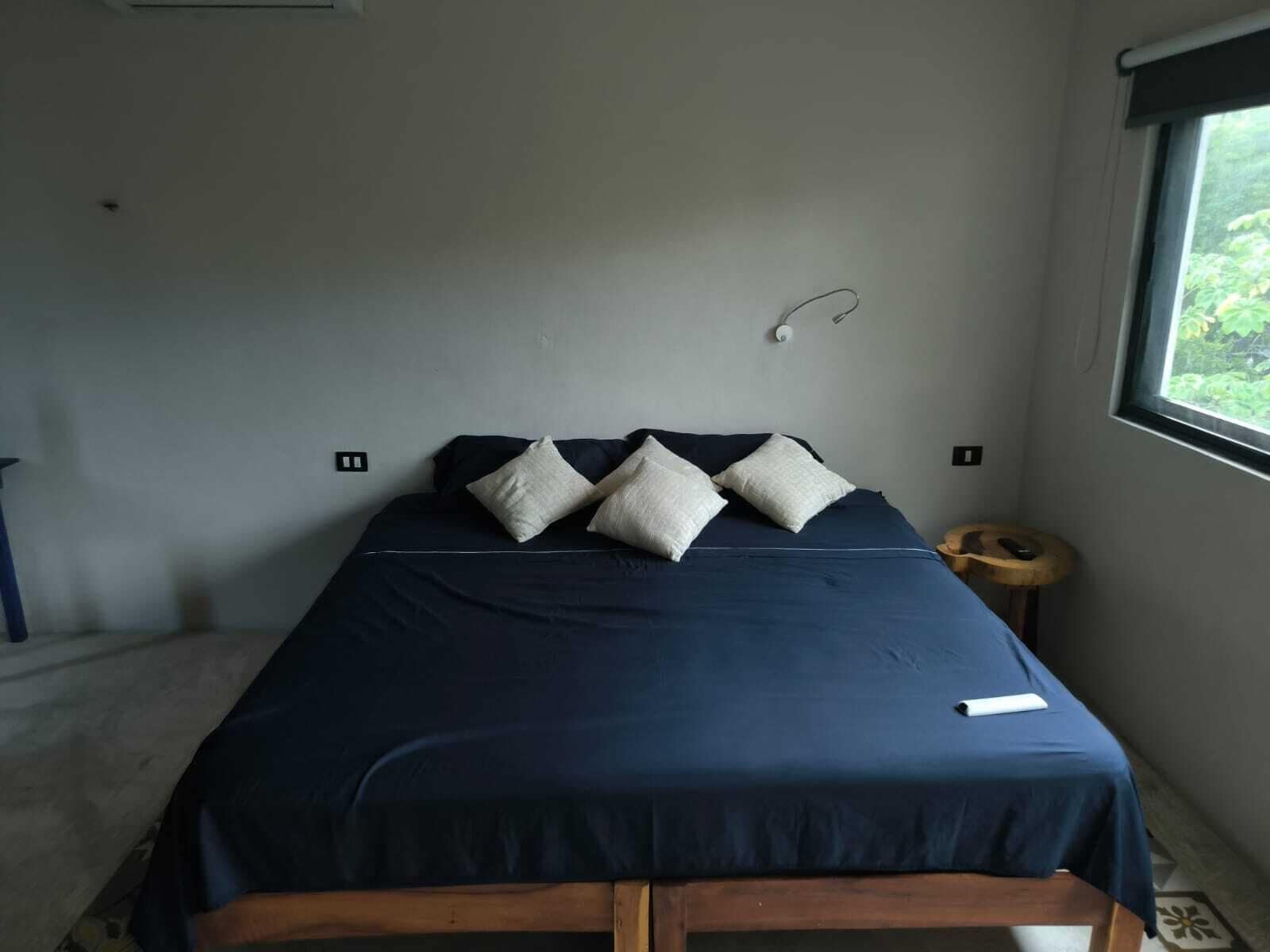 A bedroom with a bed, pillows, a bedside table, and a window.