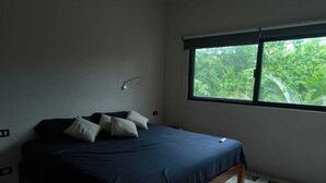 A bedroom with a bed, pillows, a window, and a view of greenery outside.