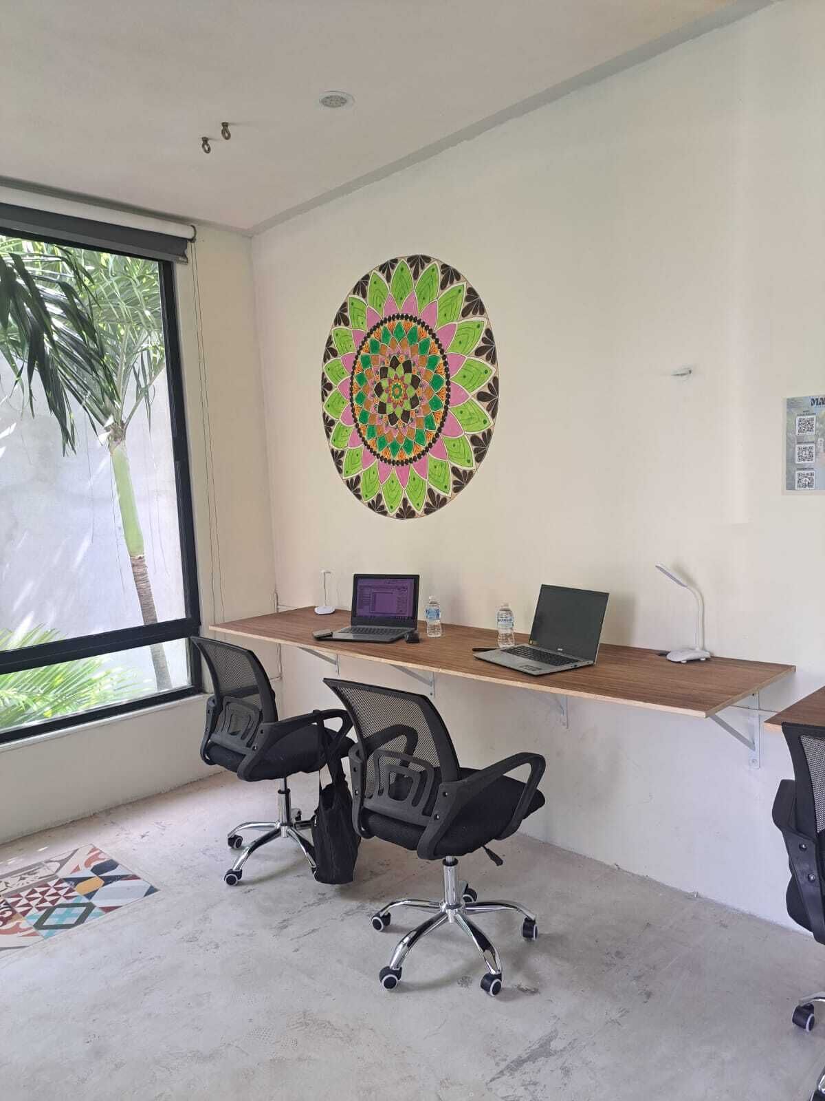Een kantoor met een groot raam, twee bureaus met laptops, twee bureaustoelen en een decoratief rond patroon op de muur.