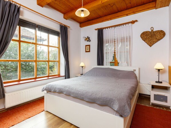 A bedroom with a large window, a bed, a nightstand, and a wall-mounted lamp.