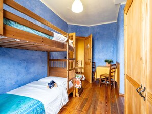Une chambre avec un lit superposé, un plancher en bois, un bureau avec une chaise et une armoire.