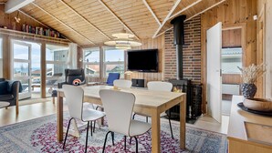 A modern living room with a wooden ceiling, a fireplace, a flat-screen TV, and a dining area with chairs and a table. - Stunning home in Sjølund with kitchen (Sjølund)