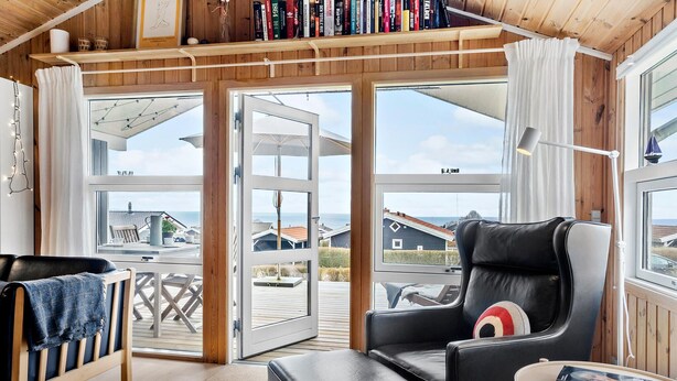 A cozy room with a black leather chair, a small table with a book, and large windows offering a view of the sea and other buildings. - Stunning home in Sjølund with kitchen (Sjølund)