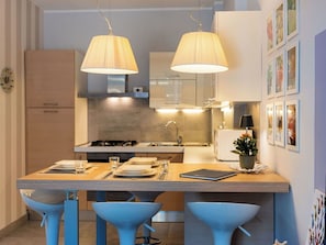 A modern kitchen with a central island, two hanging lamps, and a dining area with blue chairs.