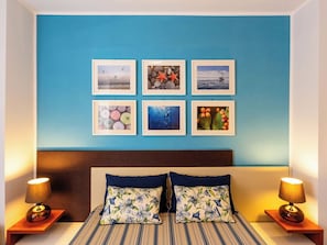 A bedroom with a blue wall, a bed with striped bedding, two nightstands with lamps, and six framed pictures.