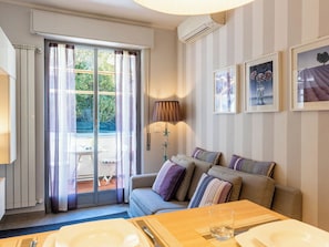 A room with a sofa, a dining table, a lamp, and a window with curtains.