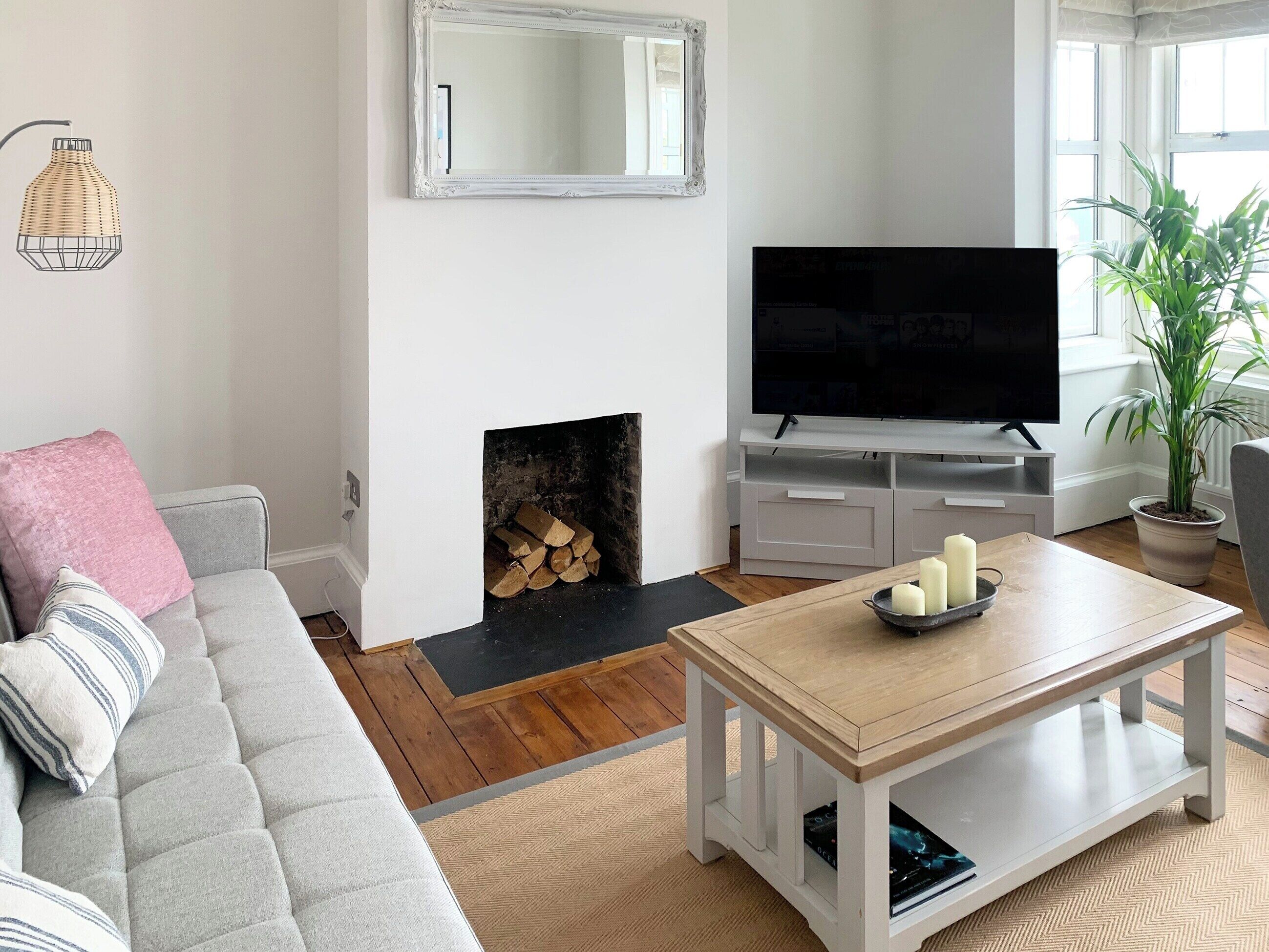 A living room with a sofa, a coffee table, a TV, a fireplace, and a potted plant.