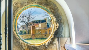 A circular window with a stone frame, revealing a view of a building and a tree. - Beautiful private villa for 3 people with A/C, WIFI, patio and panoramic view (Montescudaio)