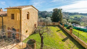 A stone building with a tiled roof, a grassy courtyard, and a view of rolling hills in the distance. - Beautiful private villa for 3 people with A/C, WIFI, patio and panoramic view (Montescudaio)