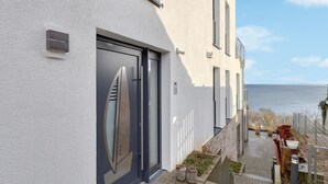 Ein modernes Gebäude mit einer großen Glasfassade, einer kleinen Außenbestuhlung und Blick auf das Meer.