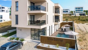 Een moderne villa met zwembad, balkons en een bordje met de tekst 'Villa Sorriso'.