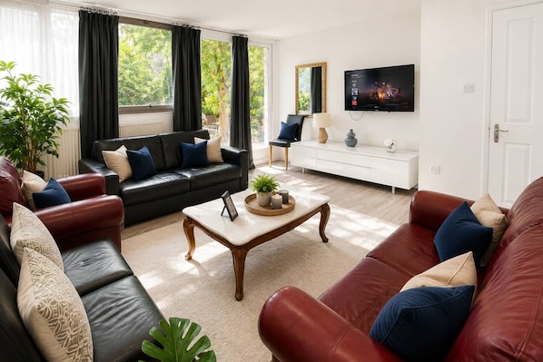 A modern living room with a black leather sofa, a red leather sofa, a wooden coffee table, and a white console table.