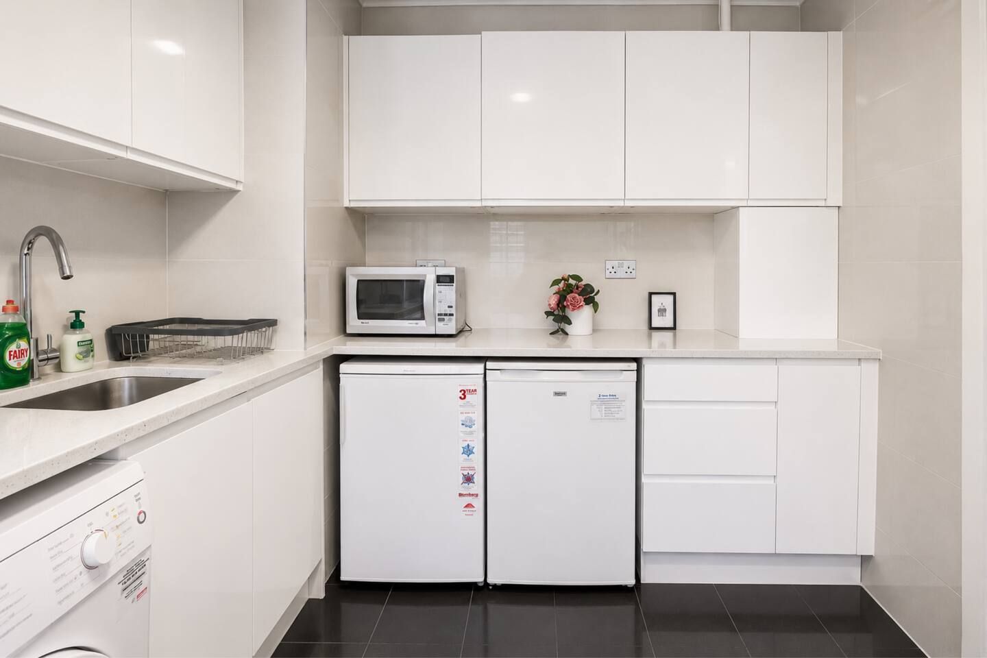 Een moderne keuken met witte kastjes, een magnetron, een vaatwasser en een spoelbak.