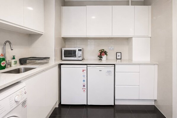 A modern kitchen with white cabinets, a microwave, a dishwasher, and a sink.