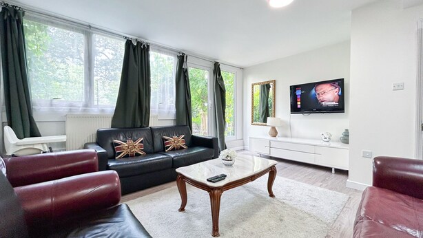 Ein modernes Wohnzimmer mit einem schwarzen Ledersofa, einem weißen Couchtisch und einem an der Wand befestigten Fernseher.