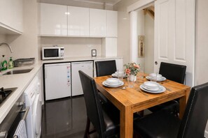 A compact kitchen with white appliances, a dining table set for four, and black chairs. - Little Venice apt near Paddington + garden & Wi-Fi (London)