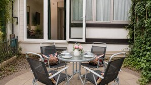 Un patio exterior con una mesa redonda, cuatro sillas y un jarrón con flores.