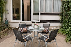 An outdoor patio with a round table, four chairs, and a vase of flowers.