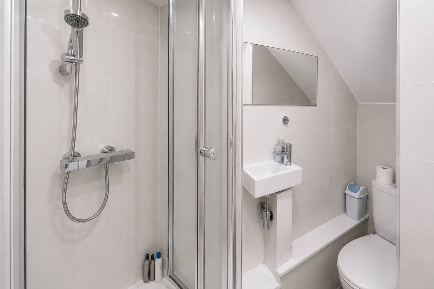 A modern bathroom with a glass-enclosed shower, a white sink, and a toilet.