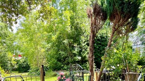 Eine Terrasse im Freien mit einem runden Tisch und vier Stühlen, umgeben von Grünpflanzen und Bäumen.