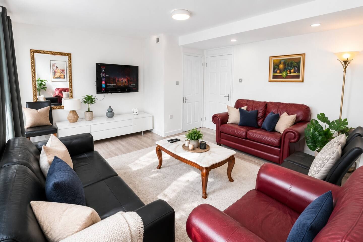 Een woonkamer met een zwarte en rode bank, een witte televisiemeubel, een flatscreen televisie en een schilderij aan de muur.
