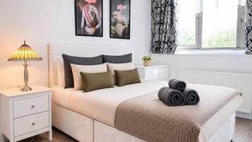 A neatly made bed with a beige quilt, a bedside lamp, and a nightstand with a drawer.