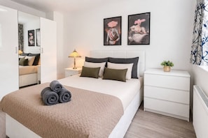 A modern bedroom with a bed, nightstands, a lamp, and artwork on the wall.