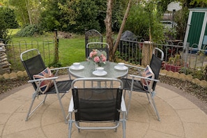 A round table with four chairs, a small vase with flowers, and a metal fence surrounding the area.