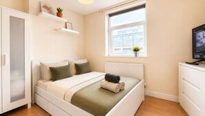 A bedroom with a bed, a radiator, a window, a TV, and a wardrobe. - 3bdr Flat Near Aldgate, Brick lane & tower hill (London)