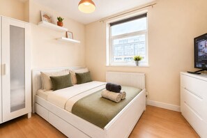 Ein Schlafzimmer mit Bett, Heizkörper, Fenster, Fernseher und Kleiderschrank.