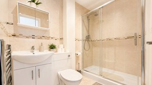 A bathroom with a glass-enclosed shower, a white sink with a mirror above it, and a toilet. - 3bdr Flat Near Aldgate, Brick lane & tower hill (London)