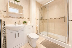 Ein Badezimmer mit einer Duschkabine, einem weißen Waschbecken mit Spiegel darüber und einer Toilette.