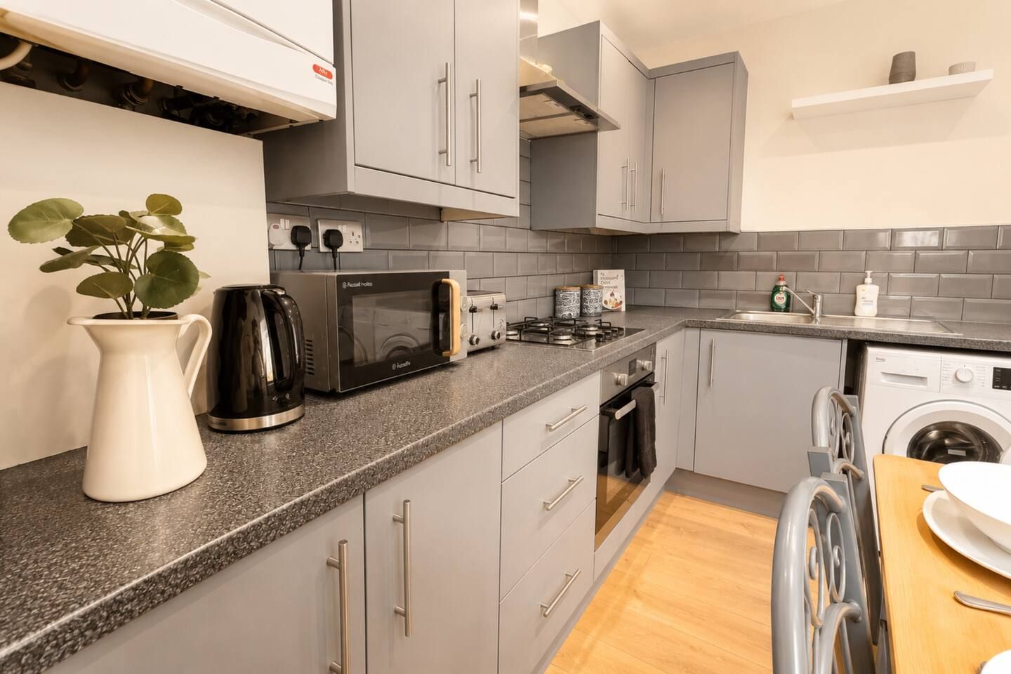 A modern kitchen with grey cabinets, a microwave, a kettle, and a washing machine.