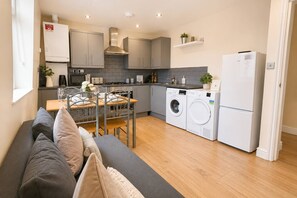 Une cuisine compacte avec des meubles gris, un lave-linge encastré et un coin repas comprenant une table et des chaises.