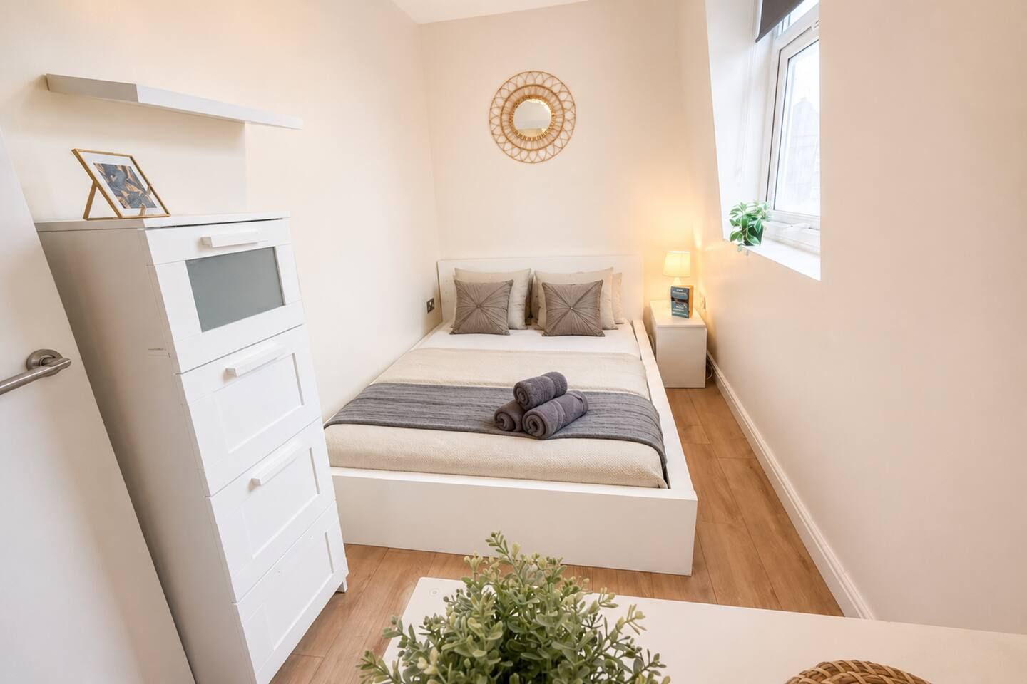 Ein gemütliches Schlafzimmer mit Bett, Nachttisch, Lampe und einer kleinen Pflanze.