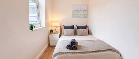 A bedroom with a bed, a nightstand, a lamp, a window, and a painting on the wall.