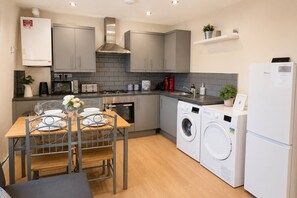 Une cuisine moderne avec des meubles gris, un four encastré, un four à micro-ondes et un lave-linge.