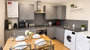 A modern kitchen with grey cabinets, a built-in oven, a microwave, and a washing machine. - 3bdr Flat Near Aldgate, Brick lane & tower hill (London)