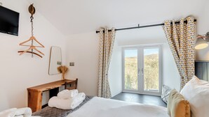 Une chambre à coucher avec un lit, un bureau, une chaise, un téléviseur et une fenêtre avec des rideaux.