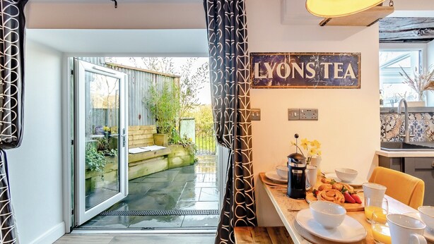 Une cuisine chaleureuse, ornée d’une enseigne indiquant « LYONS TEA », et une table à manger dressée avec des aliments pour le petit-déjeuner.