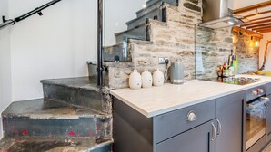 Une cuisine avec un mur en pierre, un escalier en bois et un plan de travail moderne.