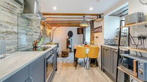 Une cuisine moderne avec un mur en pierre, des poutres en bois et une cuisinière encastrée. On y trouve deux chaises jaunes et une table à manger.