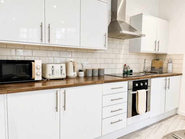 A modern kitchen with white cabinets, a wooden countertop, a microwave, a toaster, a kettle, and a dishwasher.